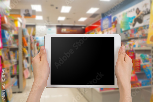 human hand hold white tablet with blank screen on blurry bookstore background.