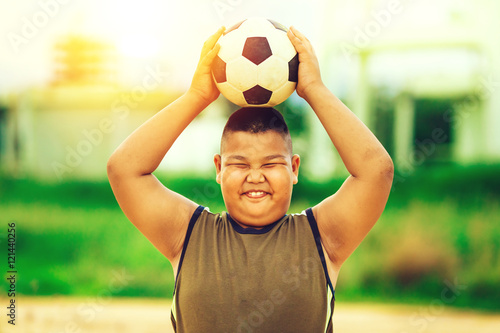 A fat boy playing soccer football for exercise under the sunlight.