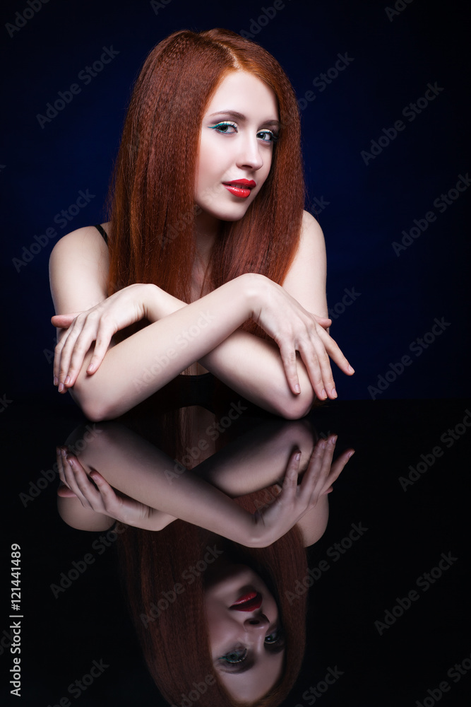 Naklejka premium Young woman with ginger hair over reflection mirror on blue back