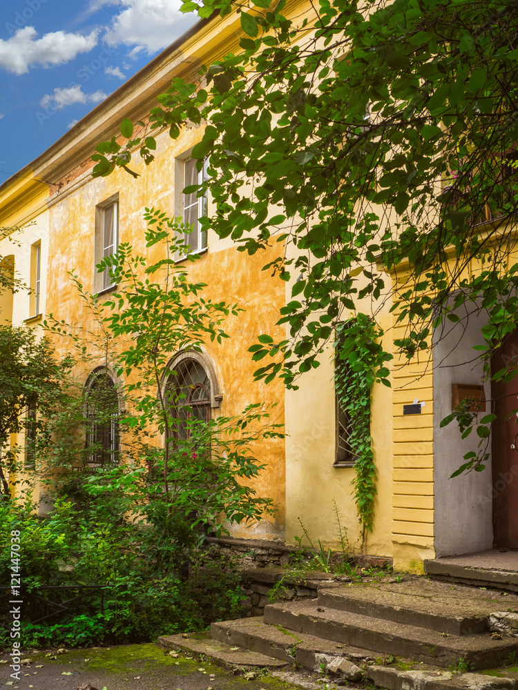 Old yellow facade in green courtyard. Beautiful old building with retro ruined porch and arched windows