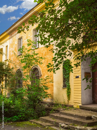 Fototapeta Naklejka Na Ścianę i Meble -  Old yellow facade in green courtyard. Beautiful old building with retro ruined porch and arched windows