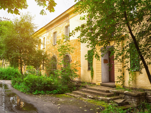 Fototapeta Naklejka Na Ścianę i Meble -  Old facade in beautiful picturesque courtyard. Yellow building with arched windows and shabby walls in the background of green plants and leaves