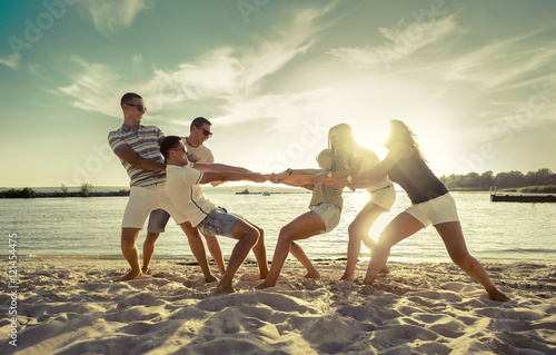 Friends funny tug of war on the beach under sunset sunlight.