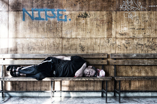 Homeless Man Sleeping on the Wooden Bench in the Train Station