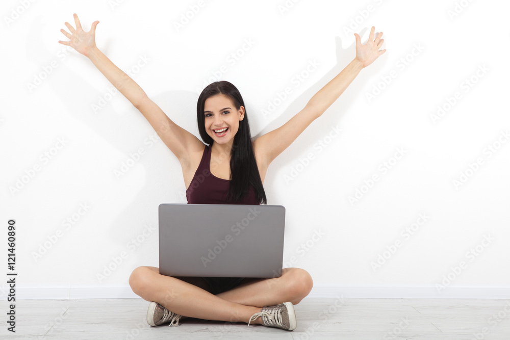 Happy young woman sitting on floor with crossed legs and using laptop on white background Happy young woman sitting on floor with crossed legs and using laptop on white background