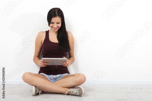 Happy young woman sitting on floor with crossed legs and using tablet, talk on Skype on white background