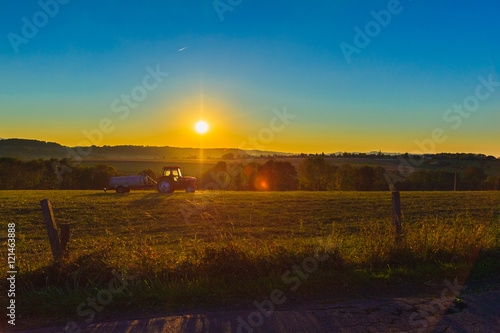 Tractor with a tank riding on field at sunset.