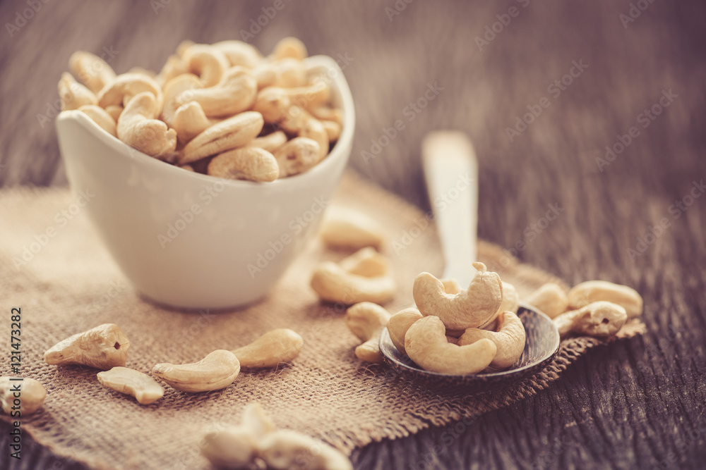 raw cashew nuts in white ceramic bowl on wood table raw cashew nuts in white ceramic bowl on wood table