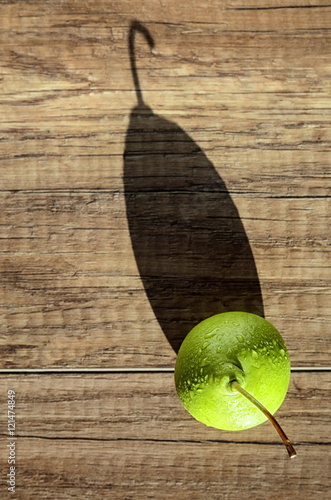 Swadow from pear. Alone juicy green pear with water drops cast a long shadow on wood background  photo