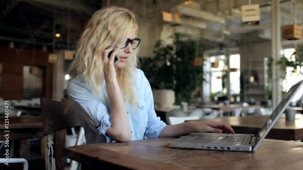 Business Woman Working at a Laptop and Phone in a Cafe Business Woman Working at a Laptop and Phone in a Cafe