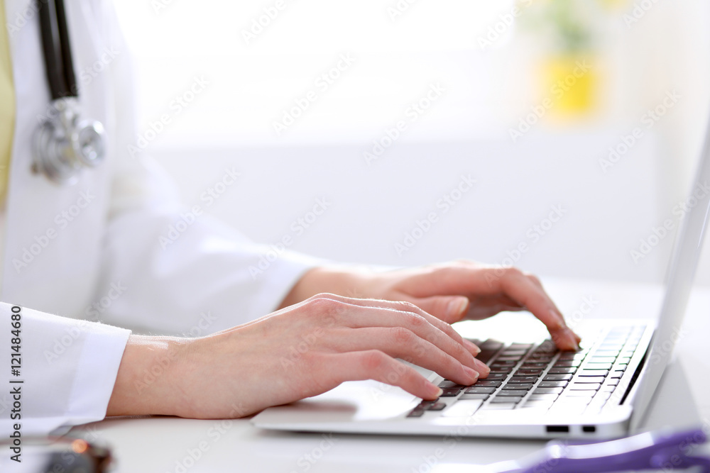 Close-up of female doctor typing laptop sitting at a table in the hospital Close-up of female doctor typing laptop sitting at a table in the hospital