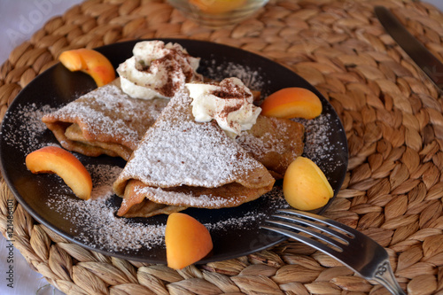 Homemade pancakes with jam, apricots, whipped cream and icing sugar.