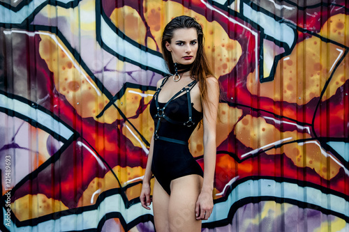 Attractive young girl with long hair wearing body posing on a background of wall with graffiti © smmartynenko