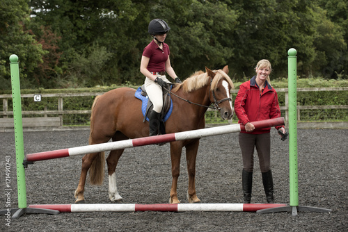 Erecting a jump in an outdoor riding school - September 2016 - Riding instructor lifting a pole to increase the height of the fence for the pupil riding a Chestnut pony