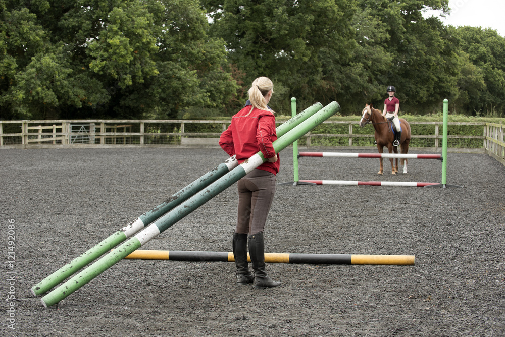 Erecting a jump in an outdoor riding school - September 2016 - Riding instructor carrying plastic poles to erect a fence in the riding school Erecting a jump in an outdoor riding school - September 2016 - Riding instructor carrying plastic poles to erect a fence in the riding school