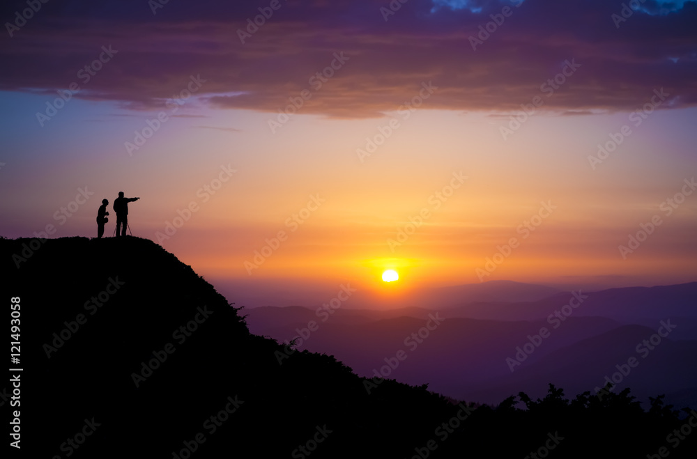 Evening landscape. Silhouettes of two people standing on a rock and looking toward the sun. Sunset in the mountains. Purple light. Summer in the Ukrainian Carpathians. With vignetting effect