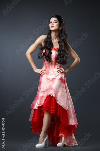 Beautiful long-haired brunette in a gypsy dress on a dark background in full length.