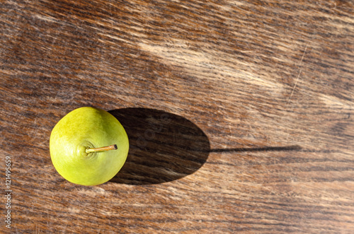 Swadow from pear. Alone juicy green pear with water drops cast a long shadow on wood background  photo