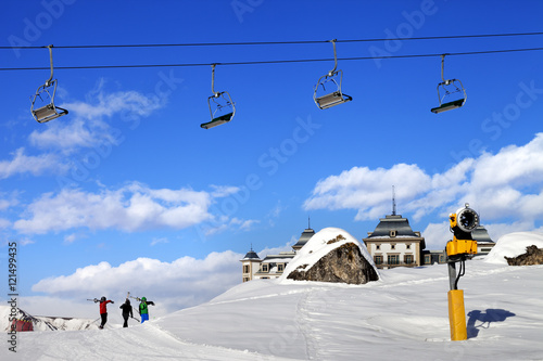 Chair-lift in blue sky and three skiers on ski slope at sun nice