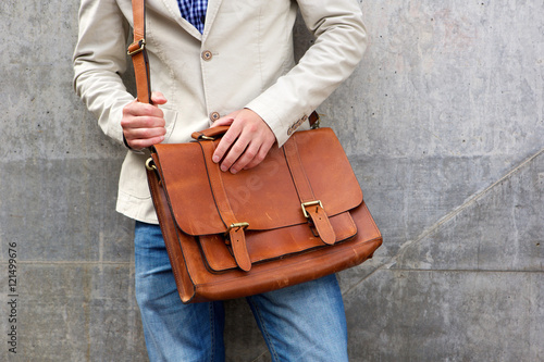 Man with leather shoulder bag standing wall