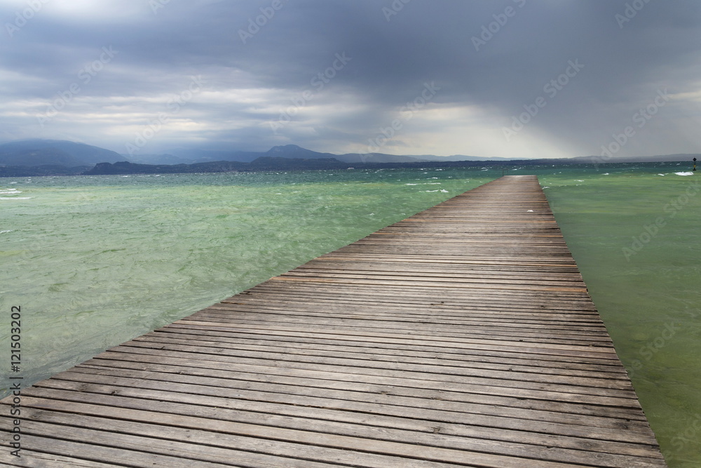 Wooden pier with waves on Lago di Garda, Sirmione, Italy