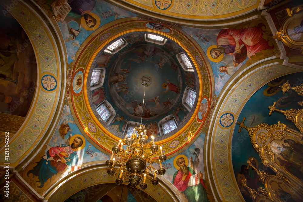 Dome of the church painted frescoes depicting holy martyrs. a large chandelier hanging in the center.