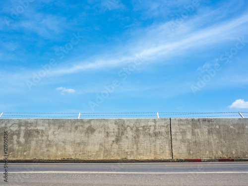 Concrete wall street with barbed wire fence under a blue sky and