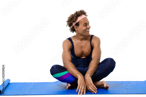 Sportive african man smiling  sitting on  karemat over white background.