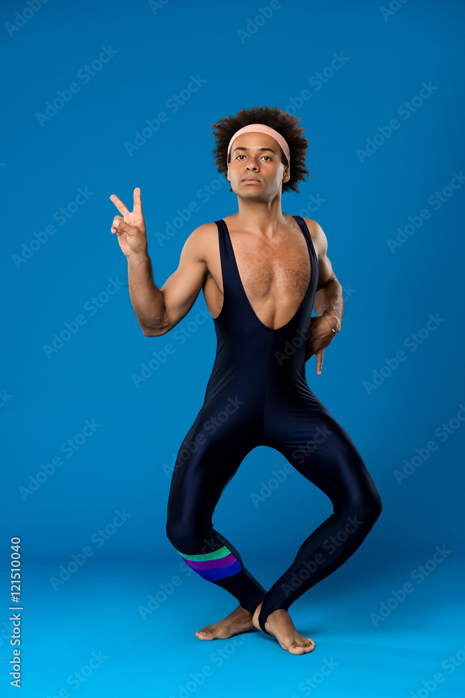 Obraz premium Sportive african man training, fooling, showing peace over blue background.