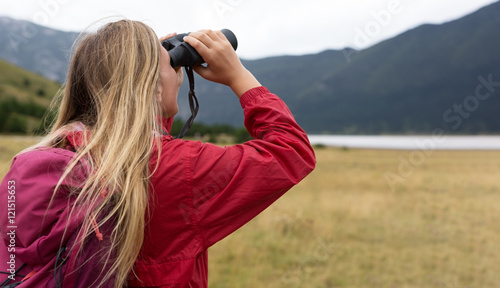 young blonde woman hiking and watching through binoculars.