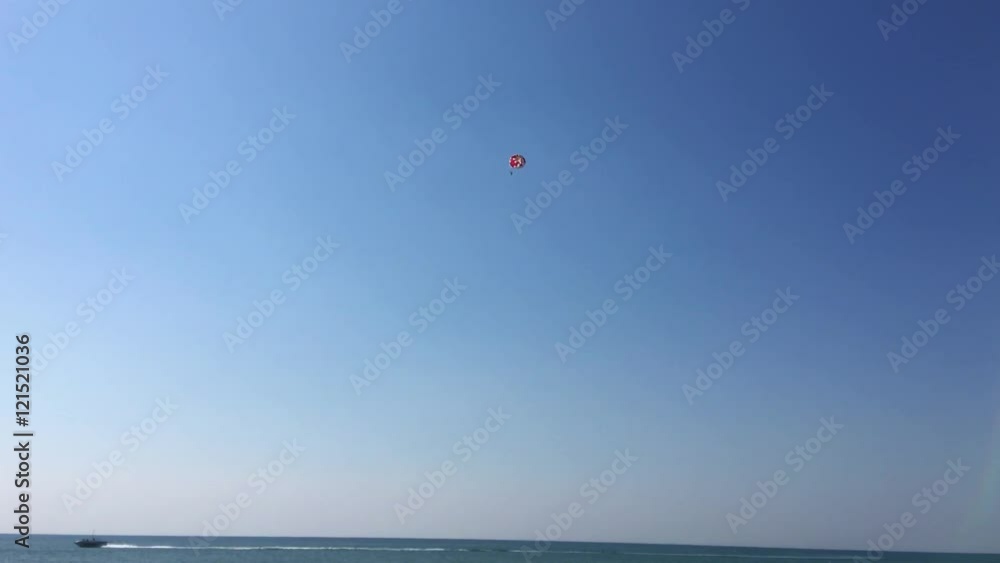 Small boat on the sea pulls the parachute against the blue sky Small boat on the sea pulls the parachute against the blue sky