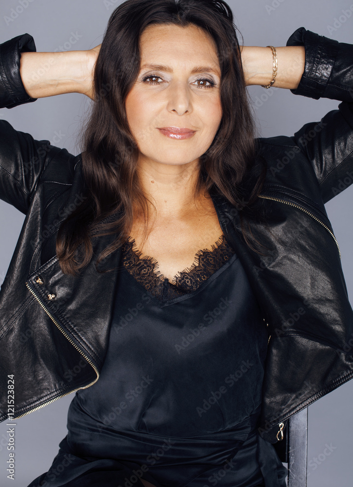 pretty brunette confident stylish real mature woman sitting on chair in  studio, sexy on gray background wearing leather jacket foto de Stock |  Adobe Stock