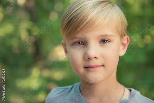 Portrait of a little boy with blonde straw hair in sunny summer day on green blurred background