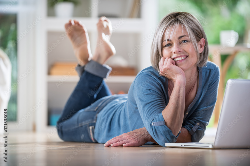 senior woman lying on wooden floor and using a laptop senior woman lying on wooden floor and using a laptop