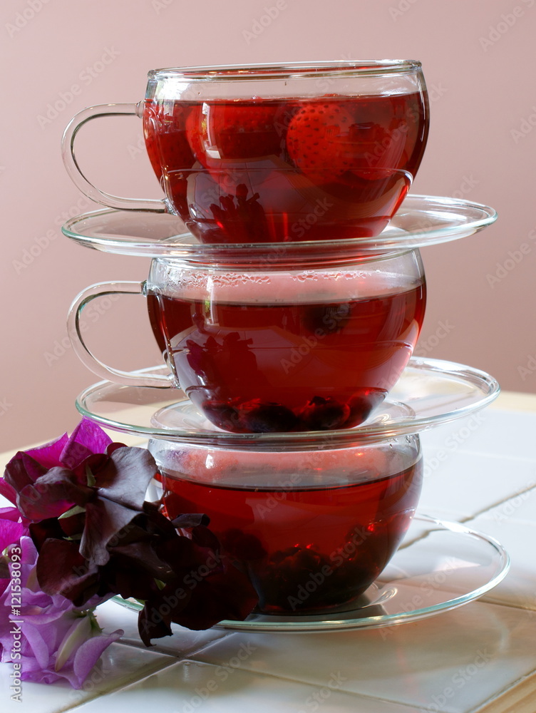 3 balanced cups and saucers of fruit tea with berries and flowers 3 balanced cups and saucers of fruit tea with berries and flowers