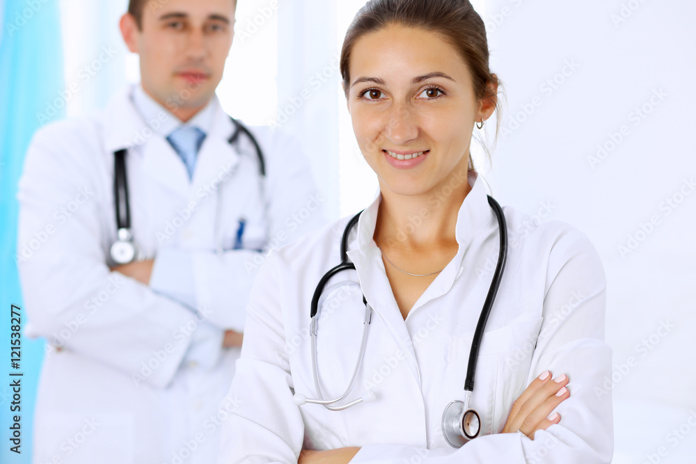 Two confident doctors standing in hospital, arms folded Two confident doctors standing in hospital, arms folded