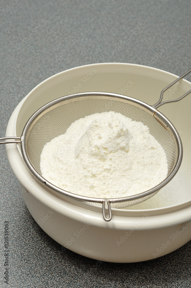 Sifting flour into a white plastic bowl