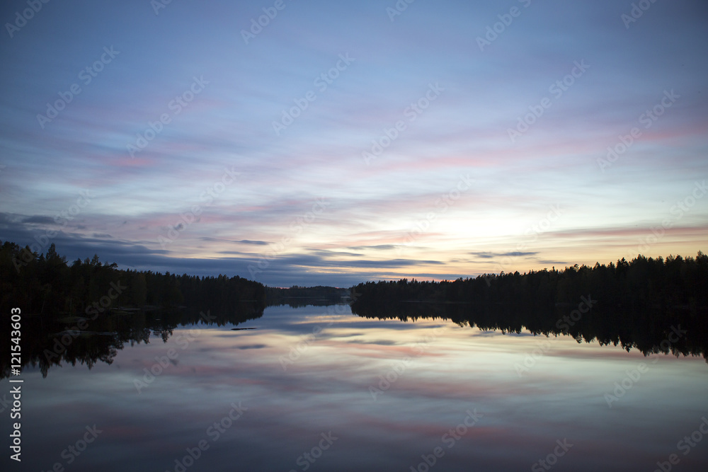 Calm evening at the lake. Some clouds are in the sky. Colorful sky. Silhouette forest.