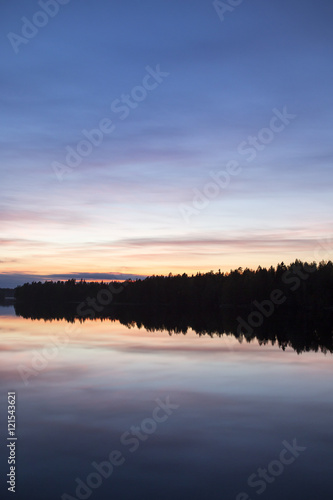 Calm evening at the lake. Some clouds are in the sky. Colorful sky. Silhouette forest.