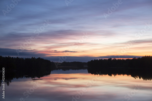 Calm evening at the lake. Some clouds are in the sky. Colorful sky. Silhouette forest.
