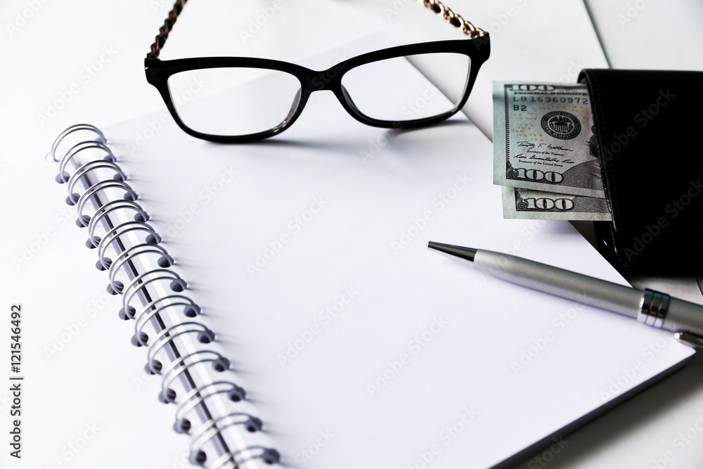 White blank notebook with silver pen and glasses. Some money and wallet are located close to it. White blank notebook with silver pen and glasses. Some money and wallet are located close to it.