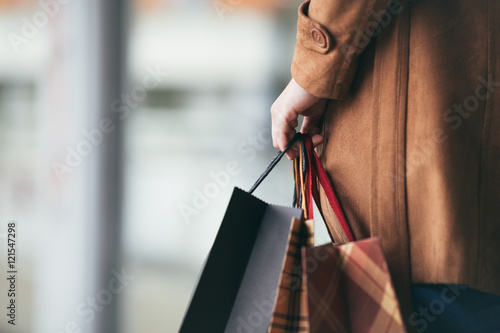 фотографія Elegant and modern woman in brown leather jacket or topcoat standing on the city street and holding bunch of shopping bags