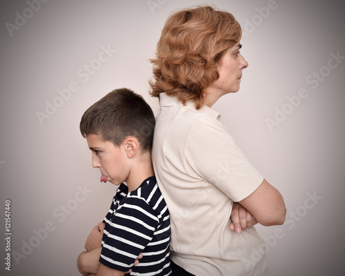 Angry mother and son sticking his tongue out with their backs to each other