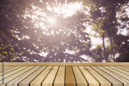 Empty top wooden table and blurred nature leave and sunrays in background. Can use for product display