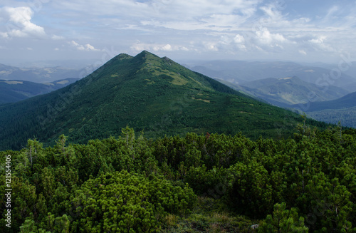 View of an overgrown mountain with three tops in cloudy summer day