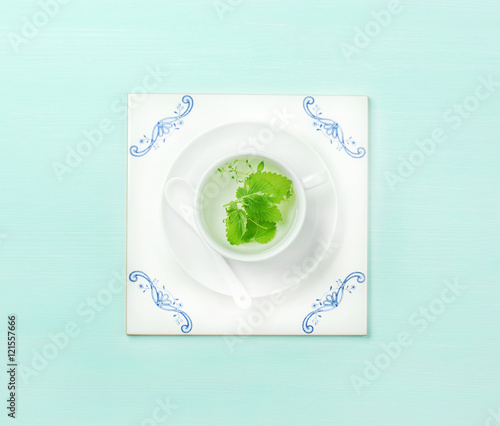 Cup of herbal tea on white ceramic tile board over mint pastel background. Top view