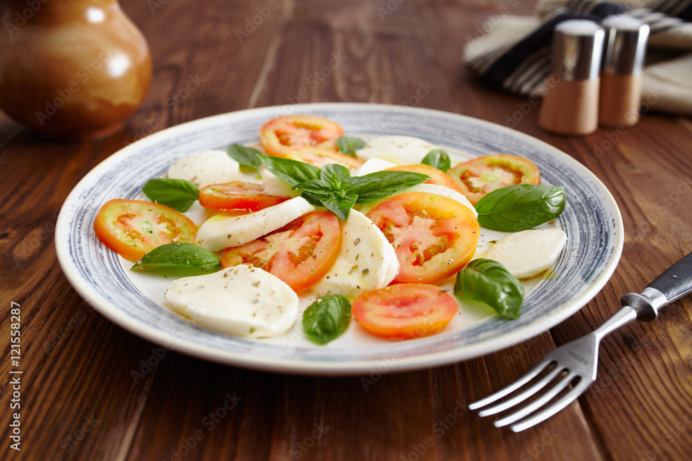Caprese salad in a blue pastel plate on an old wooden table, with salt and pepper