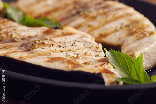 grilled swordfish slices in a cast iron pan on a wooden table, garnished with mint, oregano, salt and salmoriglio photo