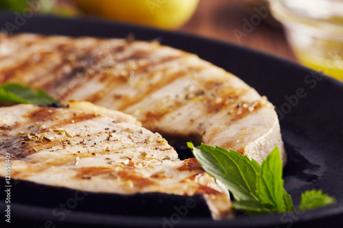 grilled swordfish slices in a cast iron pan on a wooden table, garnished with mi Fototapet