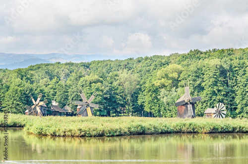 Windmill and watermill near water lake, green forest, wild vegetation